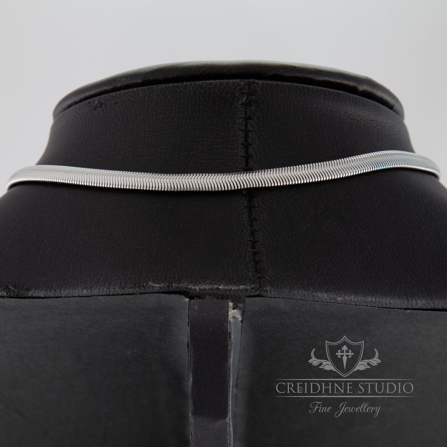 Close-up of a the back of a silver snake chain collar with a visible brand logo on a grey background