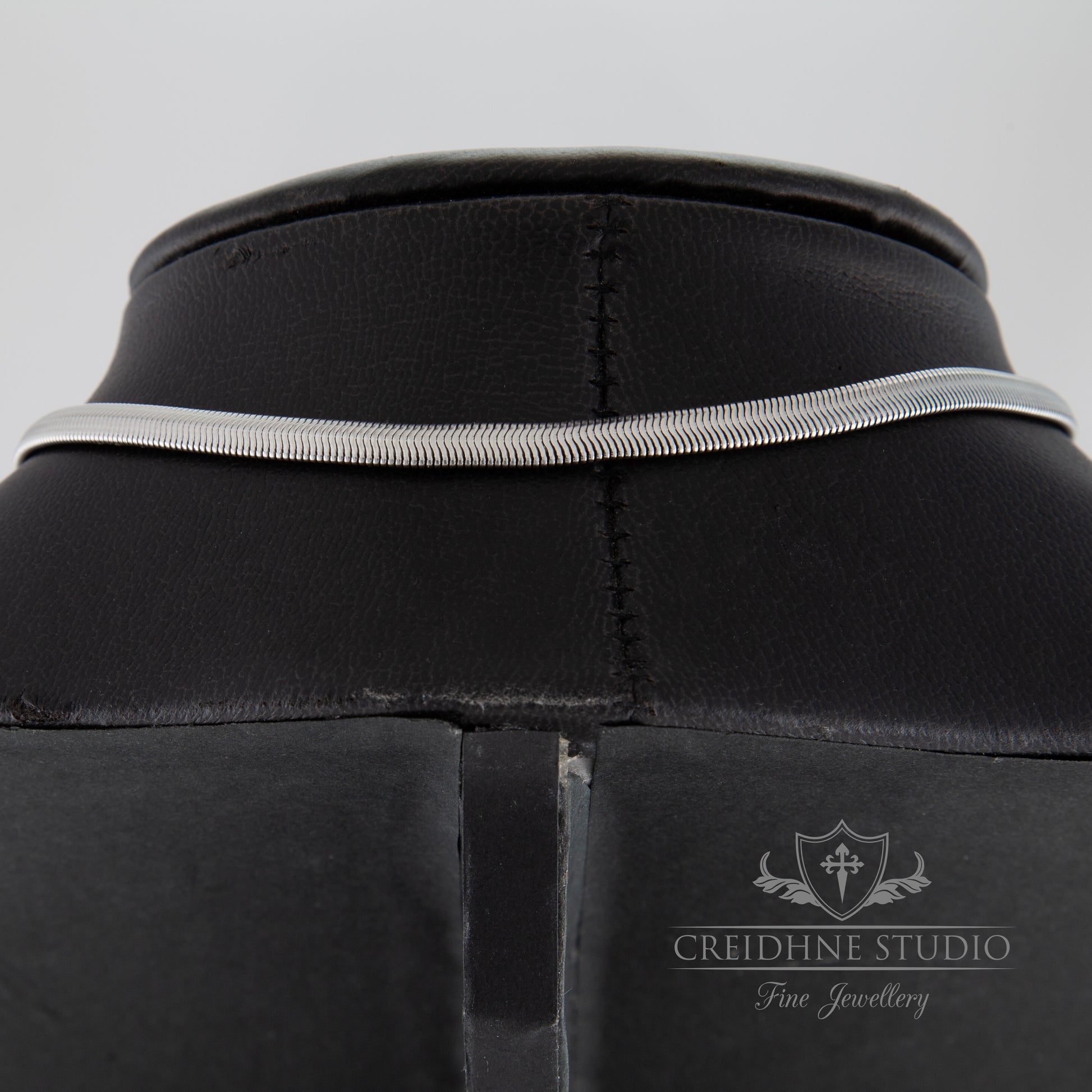 Close-up of the back of a silver snake chain collar with a visible brand logo "Creidhne Studio"